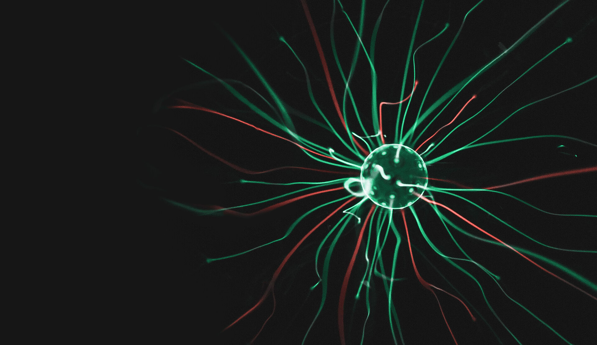 Abstrakte Darstellung einer leuchtenden Kugel mit grünen und roten Lichtlinien, die strahlenförmig nach außen verlaufen und Energie- oder Datenströme symbolisieren.