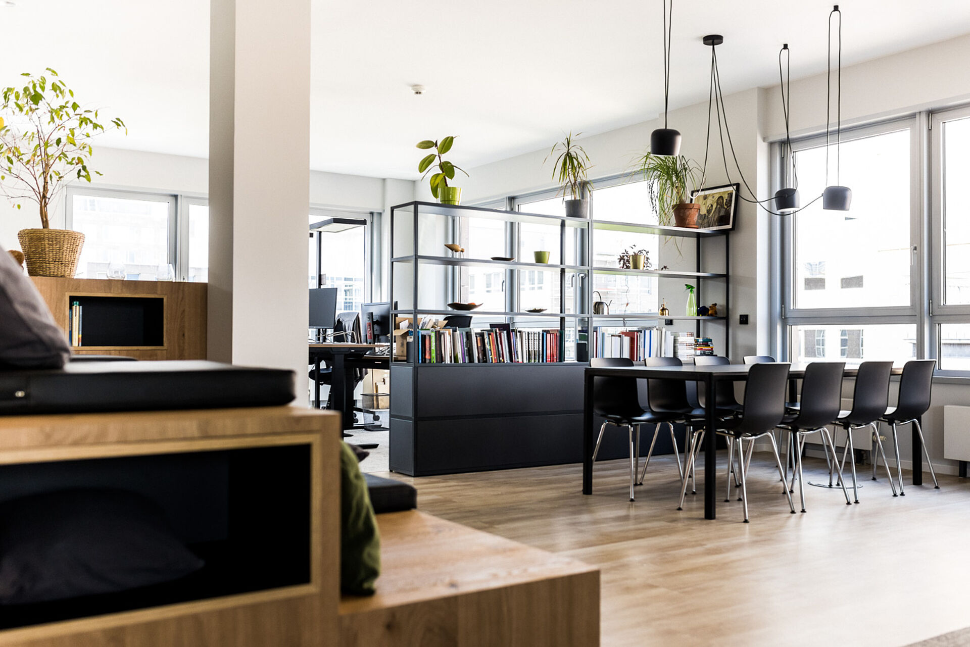 Heller Besprechungsraum mit langem Tisch, mehreren Stühlen, Bücherregal und großen Fenstern in modernem Büroambiente.