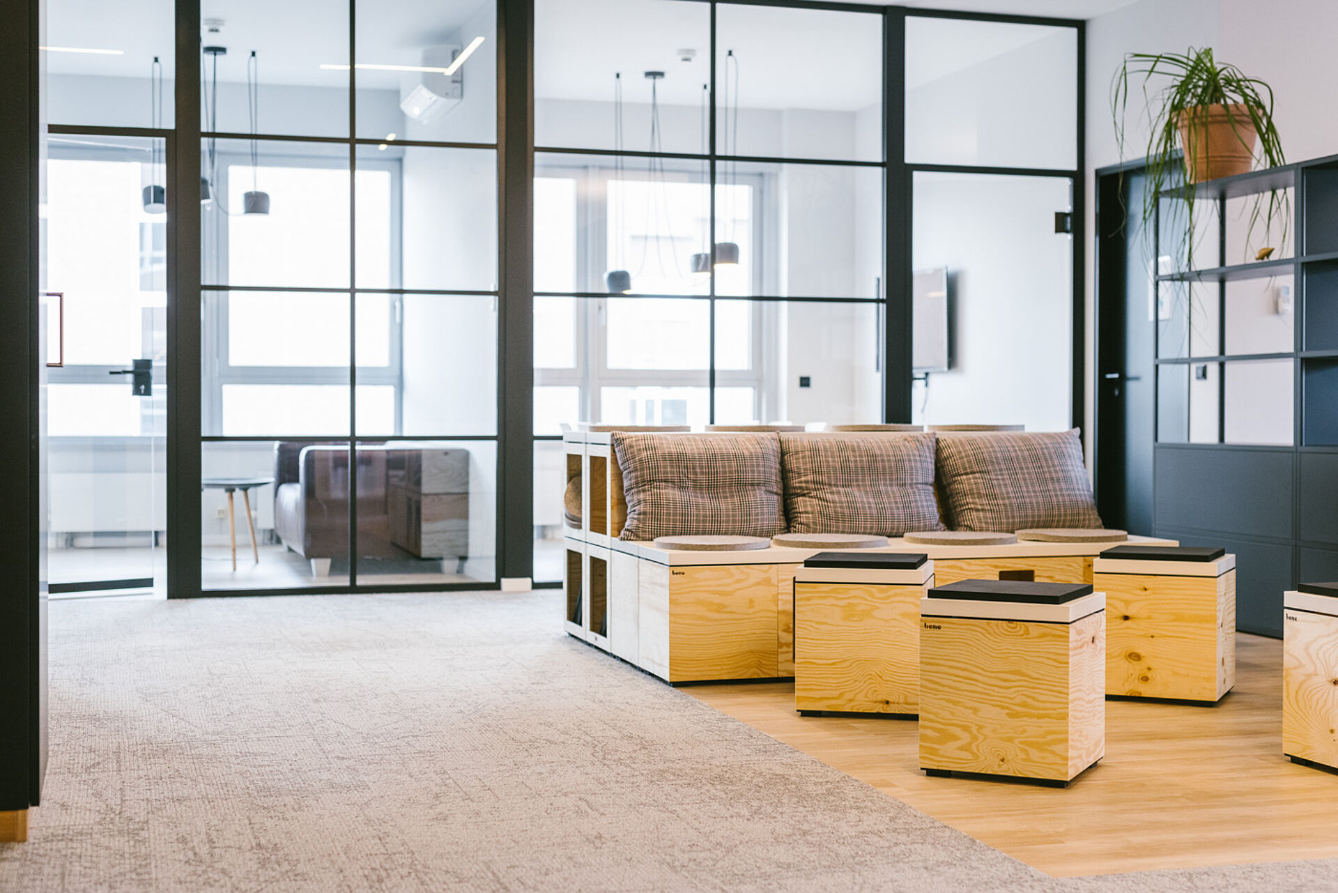 Moderner Loungebereich mit Sofa und Sitzwürfeln aus hellem Holz, kombiniert mit Textilkissen in einem offenen, zeitgemäßen Büro- oder Arbeitsumfeld.