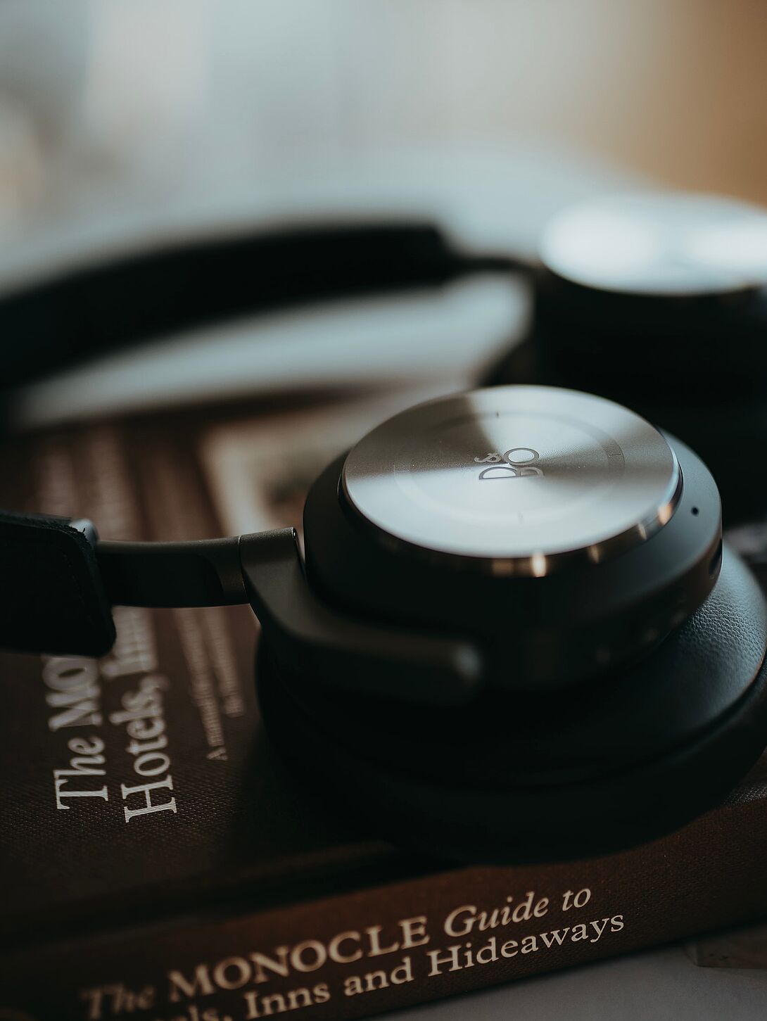Nahaufnahme von Over-Ear-Kopfhörern, die auf einem Buch liegen, mit weicher Unschärfe im Hintergrund und dezenter farblicher Überlagerung.