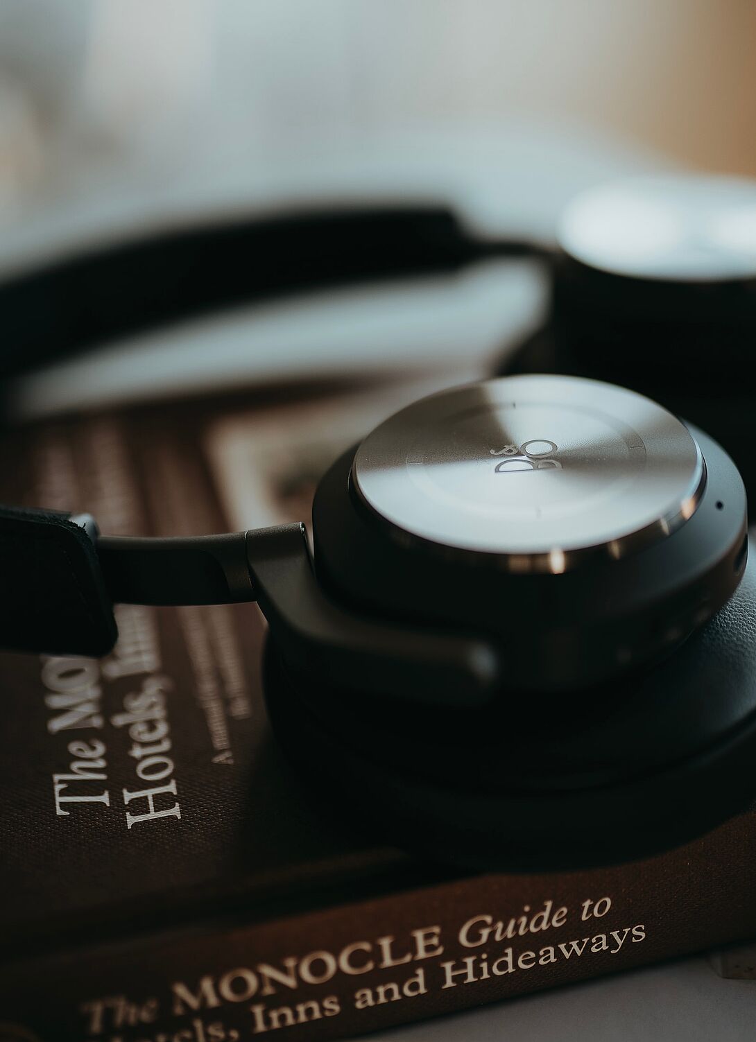 Nahaufnahme von schwarzen Over-Ear-Kopfhörern, die auf einem Buch liegen, mit weicher Tiefenunschärfe und dezenter farblicher Überlagerung.